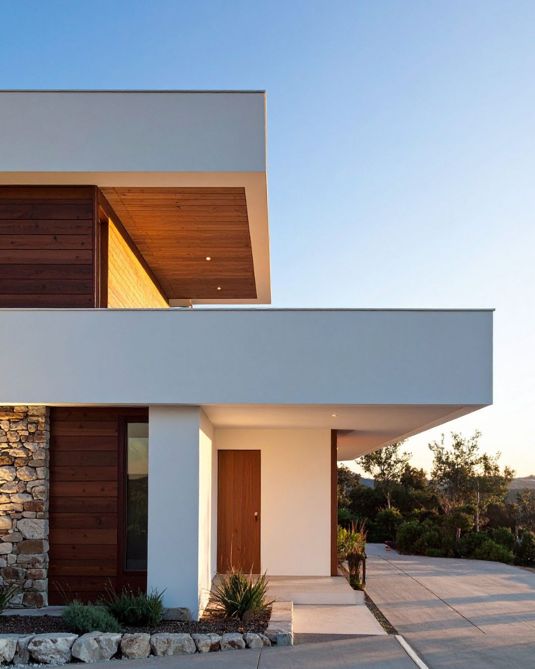 Modern white residence at sunset with wood and stone accents.