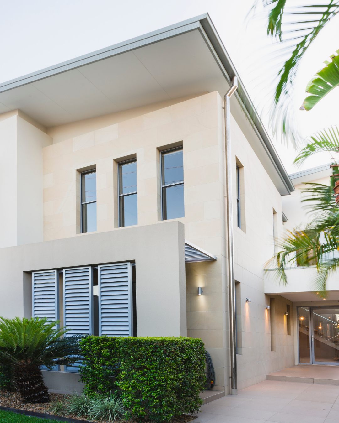 Sandstone home with louvered shutters and tropical landscaping.